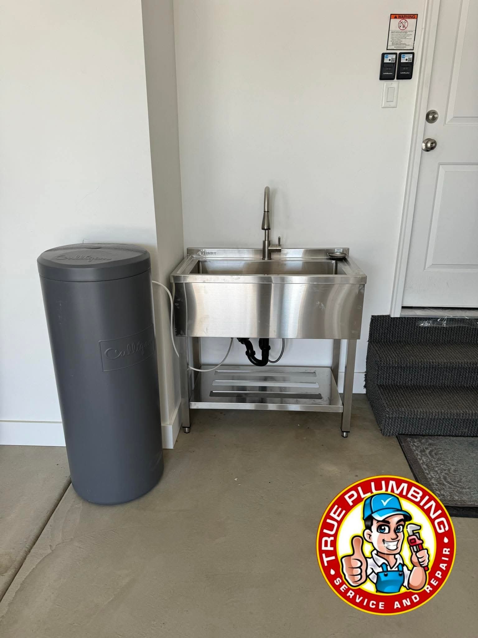 Plumber installing utility sink with drain and water supply connections in garage